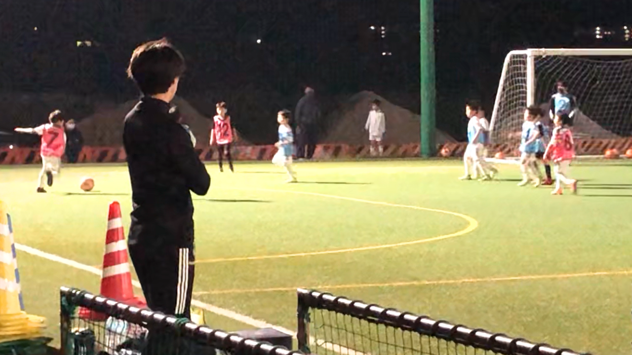 少年サッカーの練習を見守るコーチとプレーする子どもたち