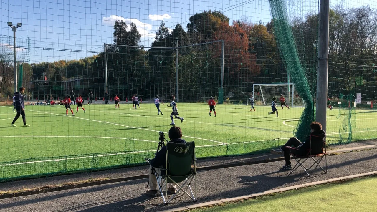 少年サッカーの試合をピッチ外から見守る保護者の様子。試合中の指示をやめて子どもの判断を見守る記事の画像